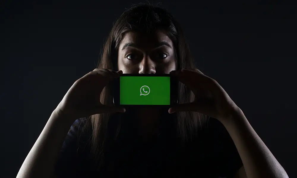 Frau mit Mobiltelefon vor Ihrem Mund mit dem WhatsApp Logo am Display